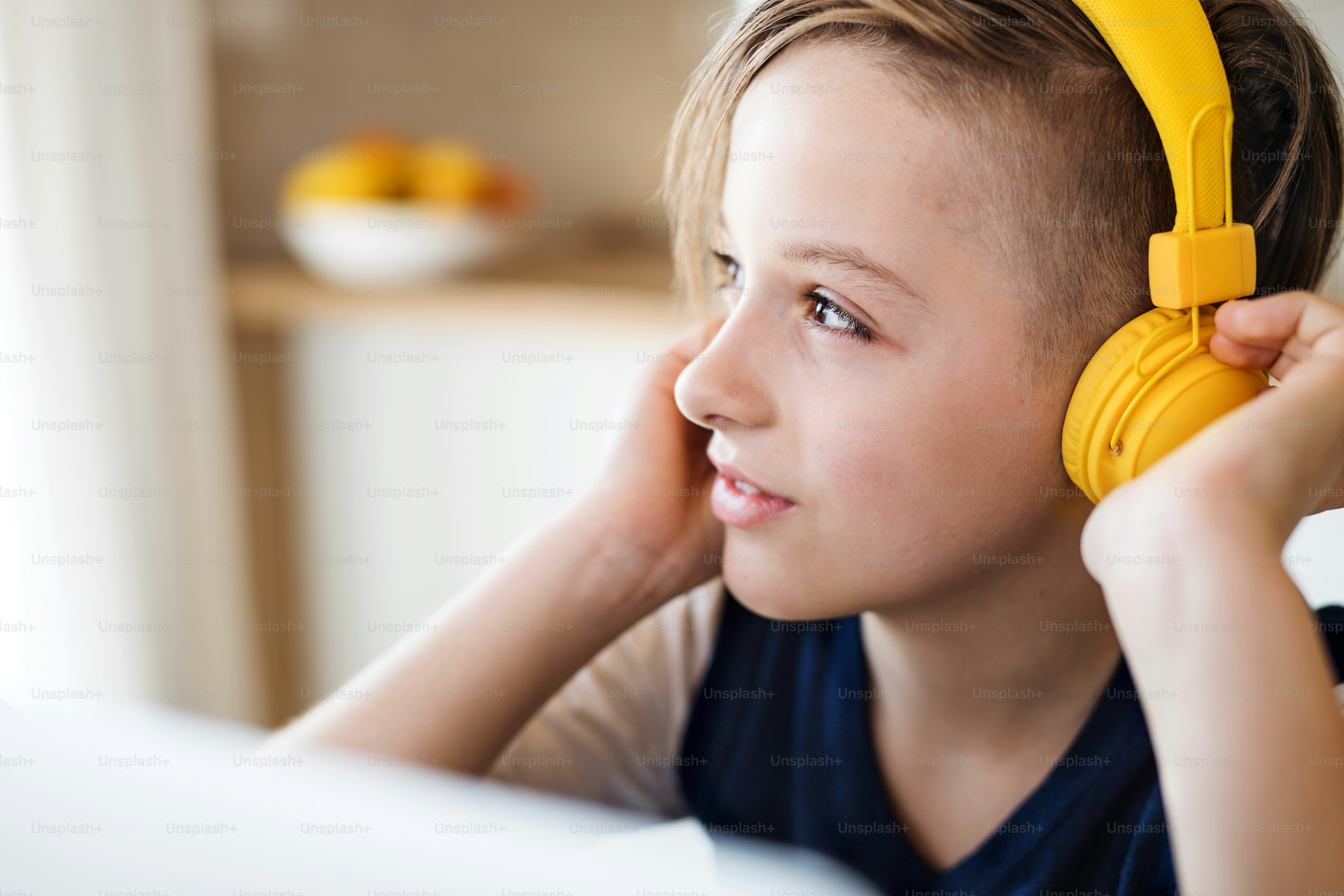 A small boy with headphones and laptop sitting at the table indoors at home.