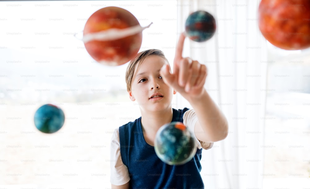 A small boy with model of solar system indoors, working on school project.