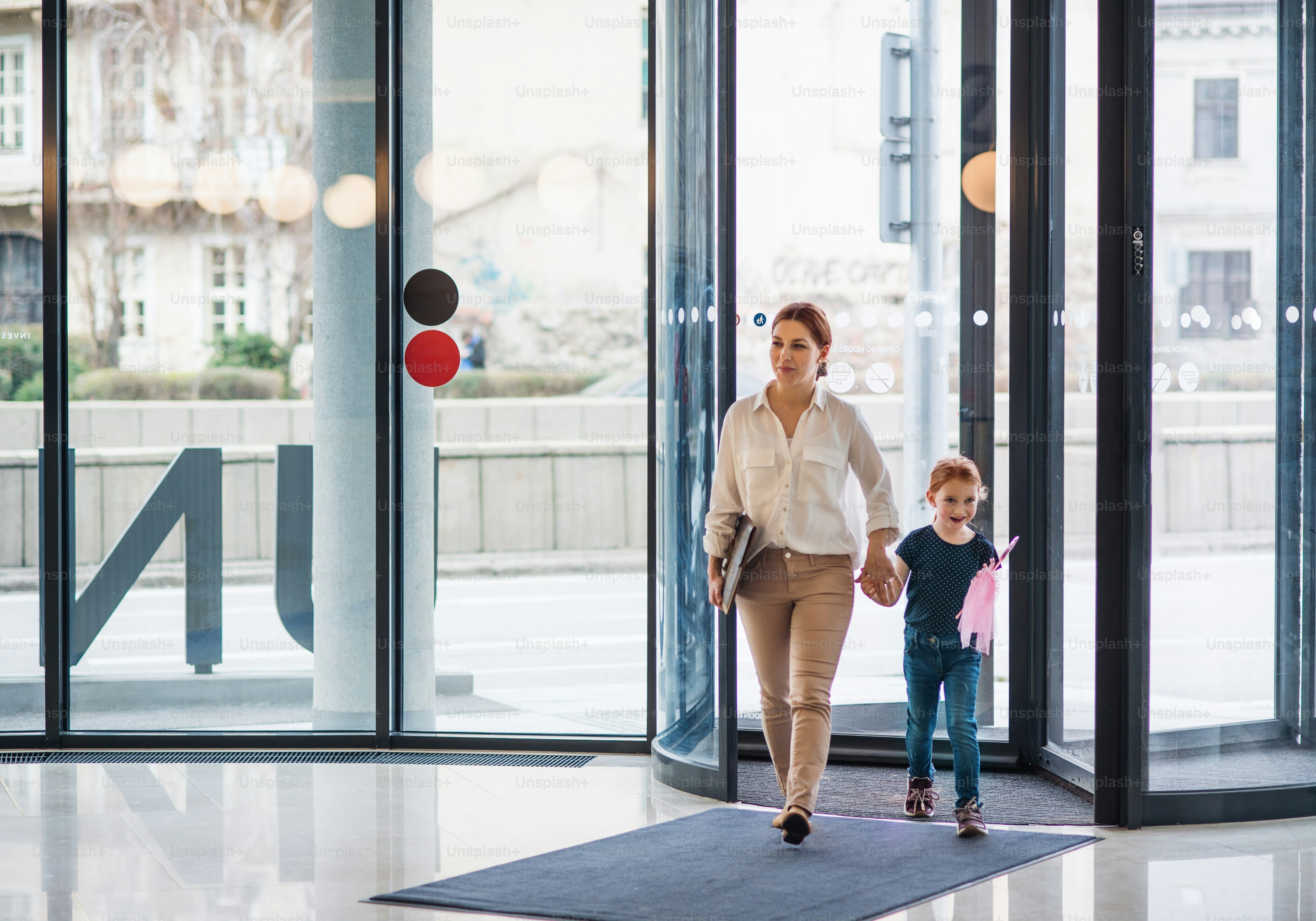 A businesswoman with small daughter entering office building, walking and holding hands