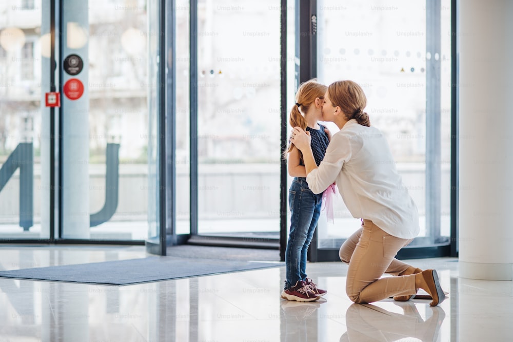 Une mère disant au revoir à une petite fille dans un immeuble de bureaux, concept de crèche.