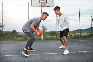 두 명의 잘생긴 십대 소년이 놀이터에서 야외에서 농구를 하고 있다.