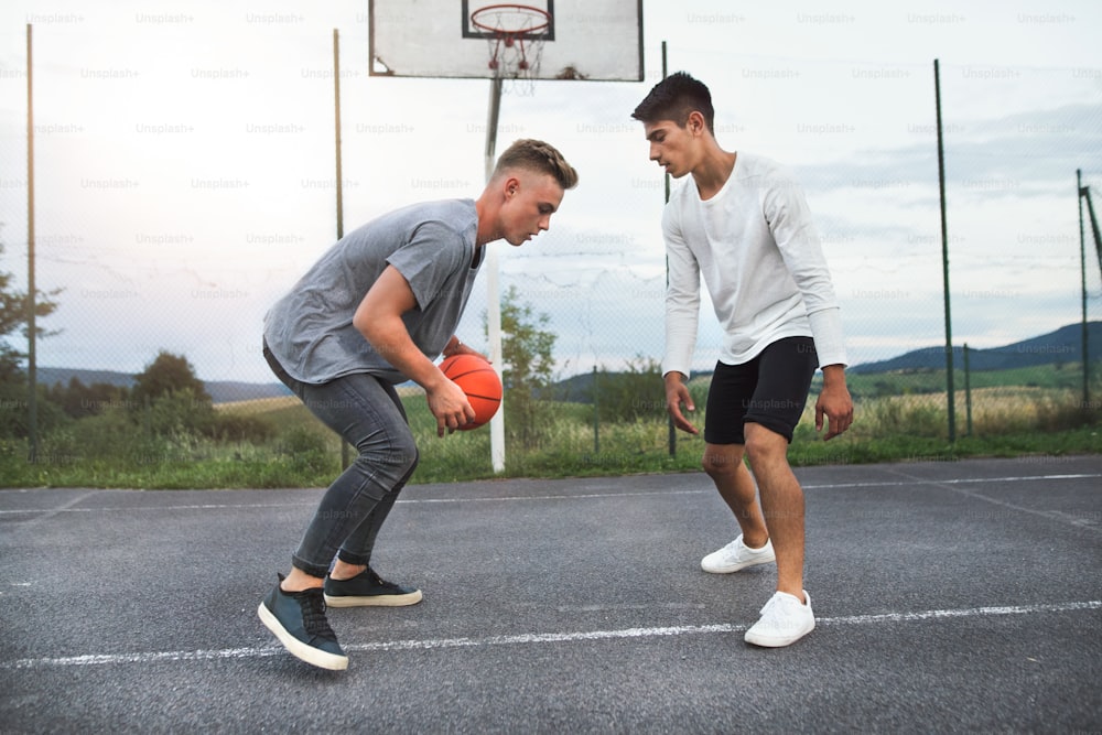 遊び場で屋外でバスケットボールをする2人のハンサムな10代の少年。