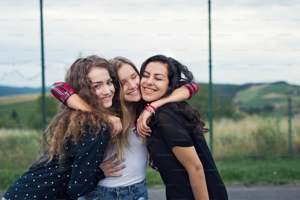 Three attractive teenage girls outdoors on playground hugging.