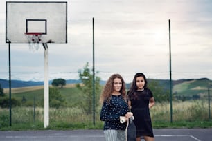 Two attractive teenage girls outdoors on playground with skateboard.