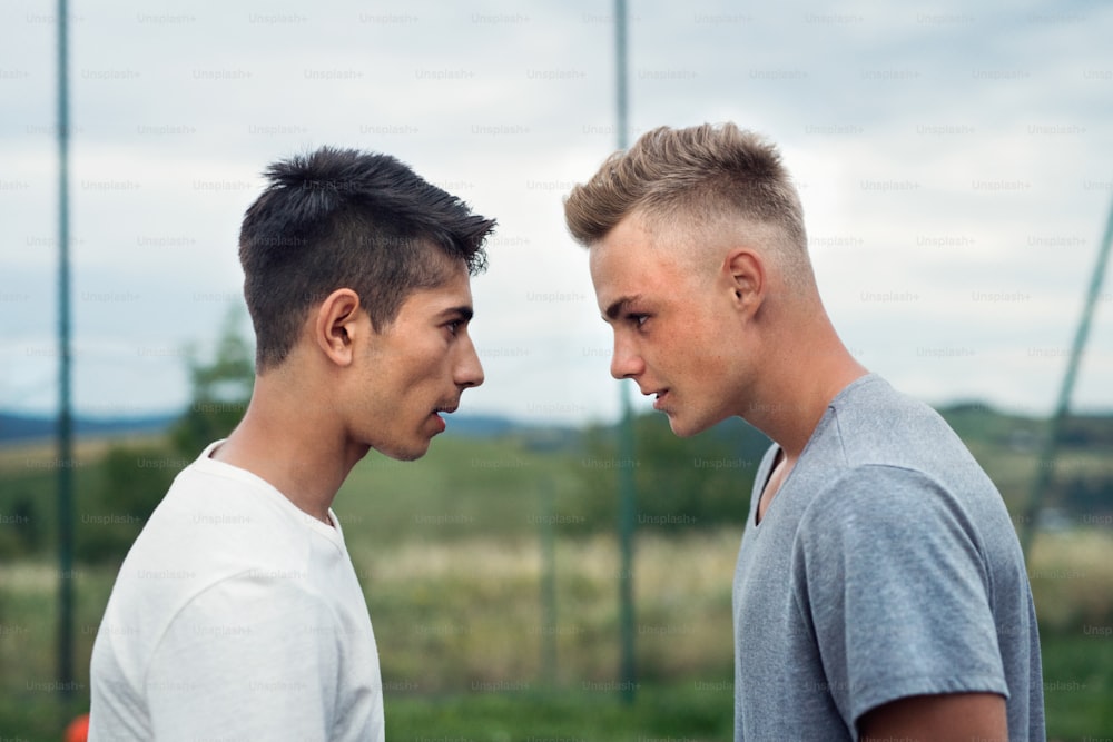 Two handsome teenage boys outdoors on playground looking at each other with hate, rivals accepting challenge.