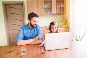 Father and daughter together, playing on laptop, sitting at the kitchen table