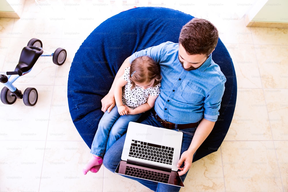 Father and daughter together, playing on laptop, sitting on bean bag, high angle view