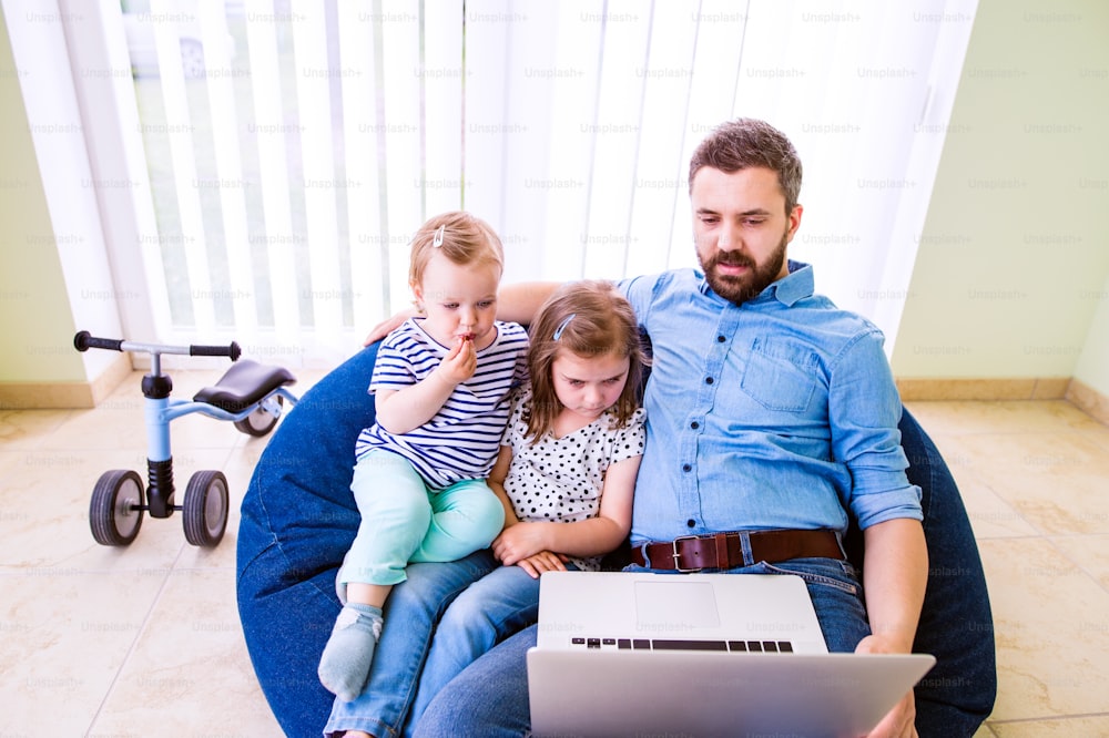 Father and daughters together, playing on laptop, sitting on bean bag, high angle view