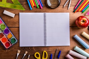 Desk with various school supplies and empty lined paper notebook  in the middle . Studio shot on wooden background, frame composition, empty copy space