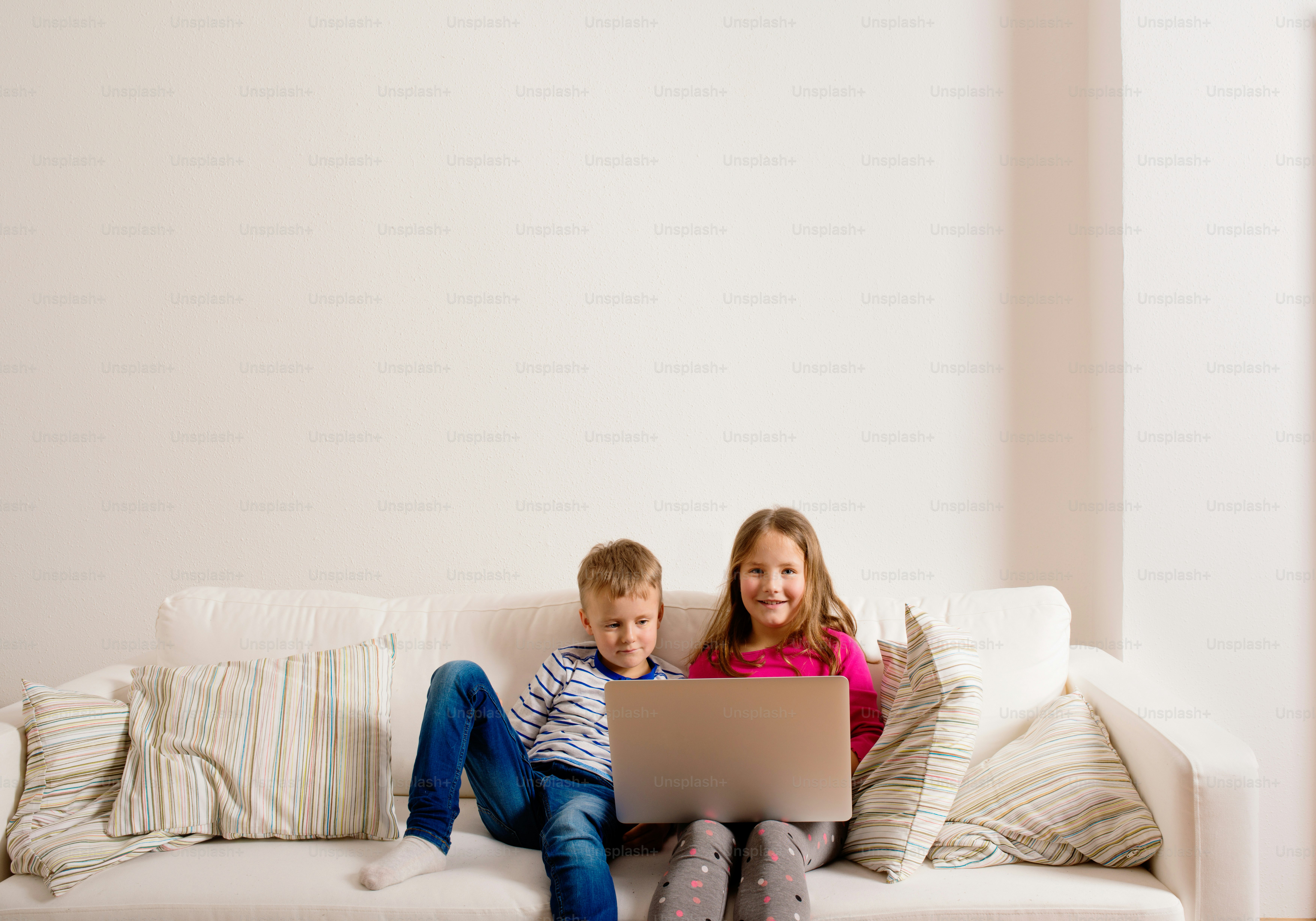 Little girl and boy sitting on sofa with a laptop computer at home. Happy children playing indoors using PC.