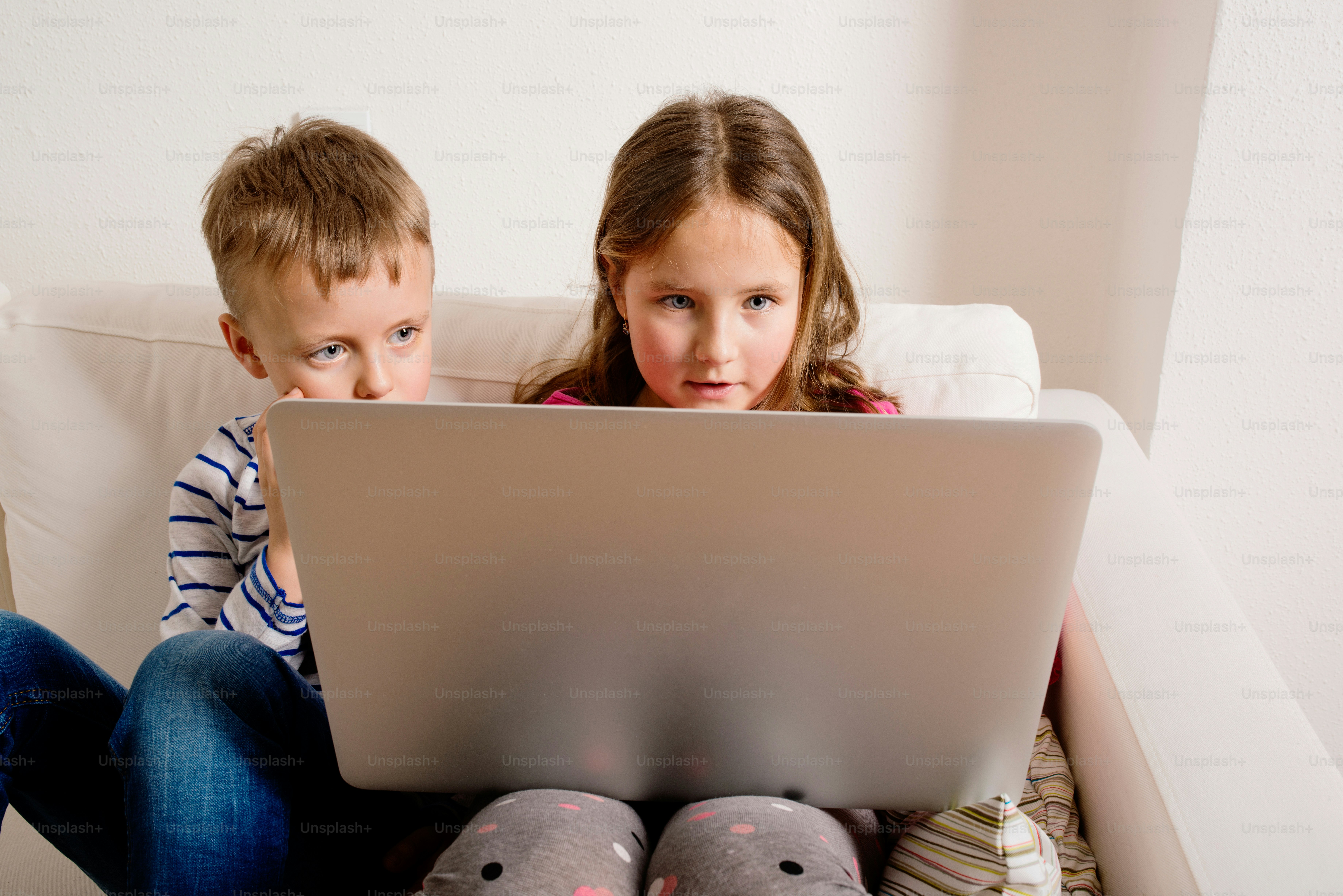Little girl and boy sitting on sofa with a laptop computer at home. Happy children playing indoors using PC.
