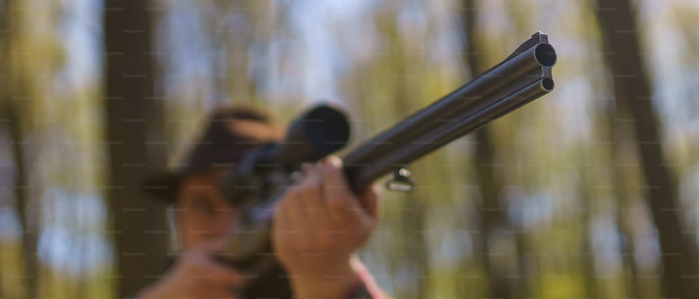 Un primer plano de un hombre cazador apuntando con pistola de rifle a una presa en el bosque.
