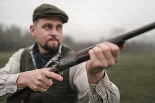 Um homem caçador em roupas tradicionais de tiro em campo mirando com espingarda.