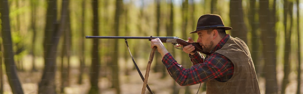Una vista lateral del hombre cazador apuntando con pistola de rifle a la presa en el bosque.