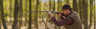 Une vue latérale d’un chasseur visant avec un fusil sur une proie dans la forêt.