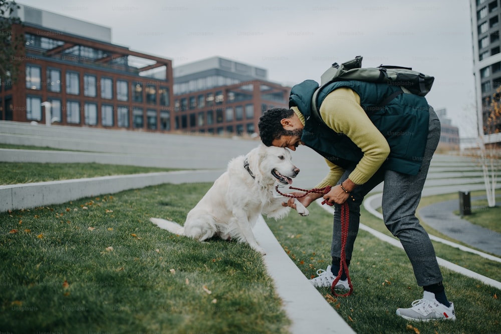 Eine Seitenansicht eines glücklichen jungen Mannes, der seinen Hund draußen in der Stadt trainiert.