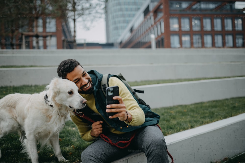 A happy young man taking selfie with his dog outdoors in town.