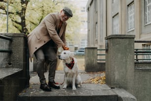 A happy senior man looking at camera during dog walk outdoors in city.