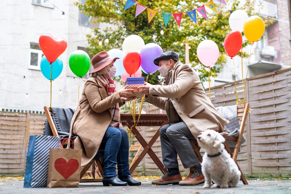 A happy senior partners in outdoor cafe in city, couple celebrating birthday. Coronavirus concept.