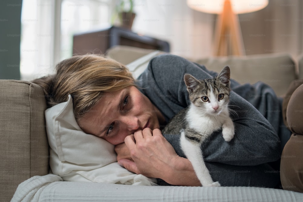 Femme avec chat à l’intérieur sur le canapé à la maison se sentant stressée, concept de santé mentale.