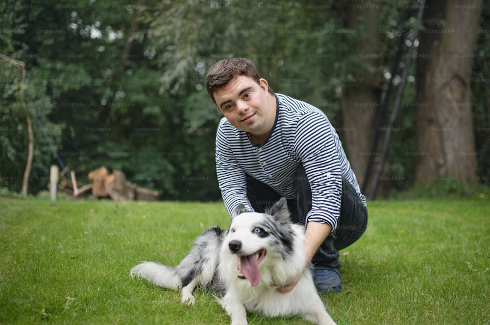 Retrato de un hombre adulto alegre con síndrome de down jugando con una mascota de perro al aire libre en el patio trasero.