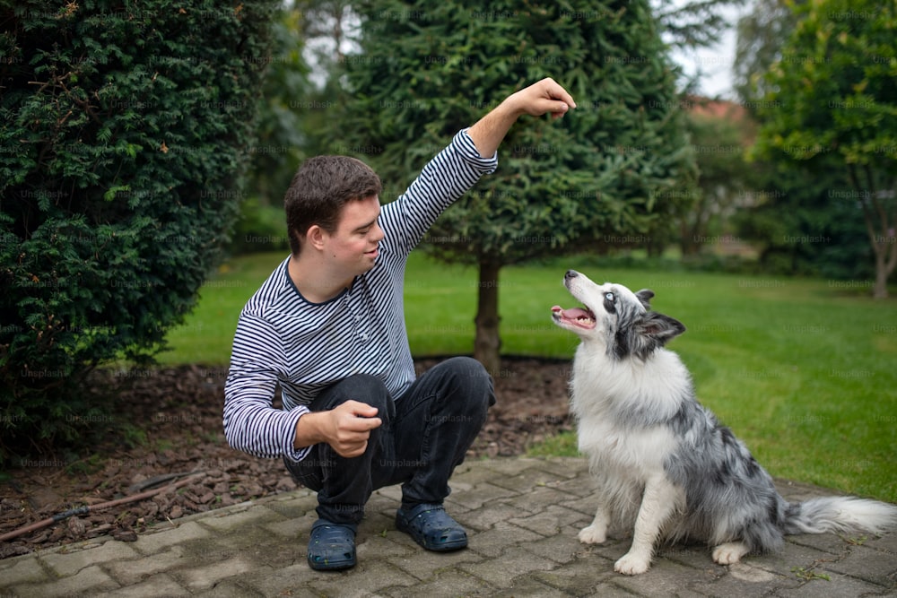 Portrait of cheerful down syndrome adult man training dog pet outdoors in backyard.