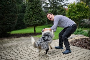 Porträt eines fröhlichen erwachsenen Mannes mit Down-Syndrom, der mit einem Hundehaustier im Freien im Hinterhof spielt.