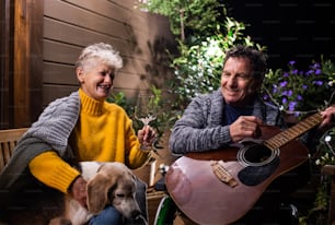 Couple senior en fauteuil roulant avec chien et guitare le soir sur terrasse, au repos.
