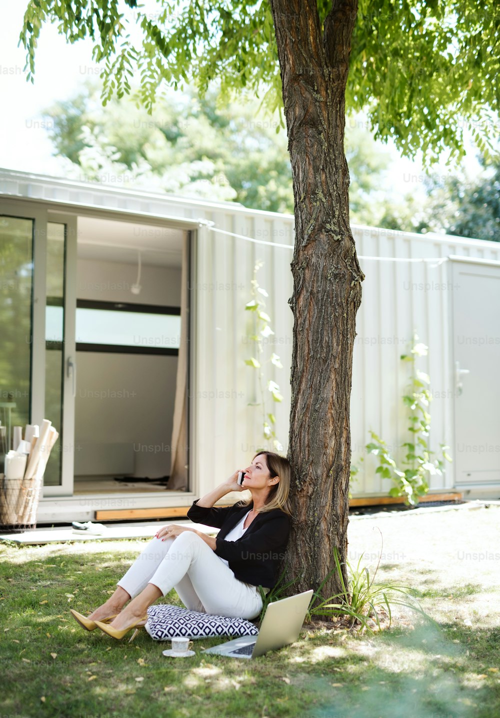 A mature woman working in home office outdoors in garden, using laptop and smartphone.