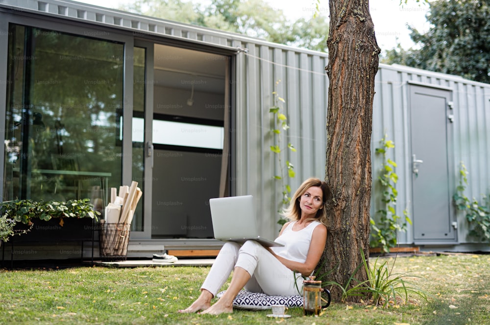 Mujer madura que trabaja en la oficina en casa al aire libre en el jardín, usando una computadora portátil.
