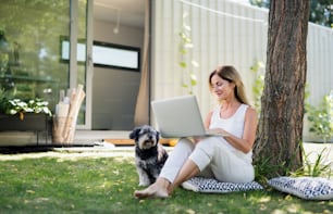 Mature woman with pet dog working in home office outdoors in garden, using laptop.