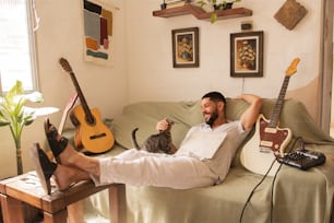 a man sitting on a couch with a guitar and a cat