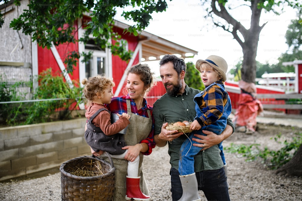 Portrait of happy family with small children standing on farm, holding basket with eggs.