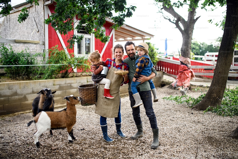 Retrato de una familia feliz con niños pequeños de pie en la granja, sosteniendo una canasta con huevos.