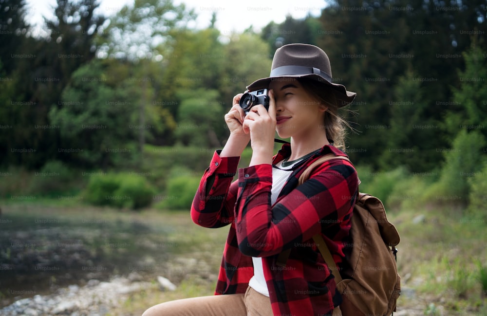 Front view of young woman with a dog on a walk outdoors in summer nature, taking photographs.