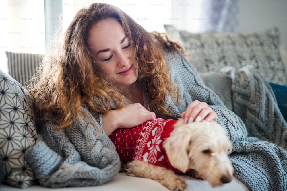 Front view of young woman relaxing indoors on sofa at home with pet dog.