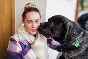 Young woman relaxing outdoors by front door at home with pet dog, looking at camera.