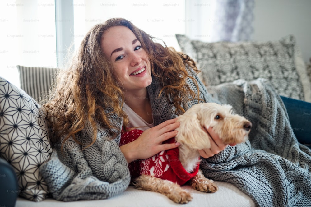Front view of young woman relaxing indoors on sofa at home with pet dog.