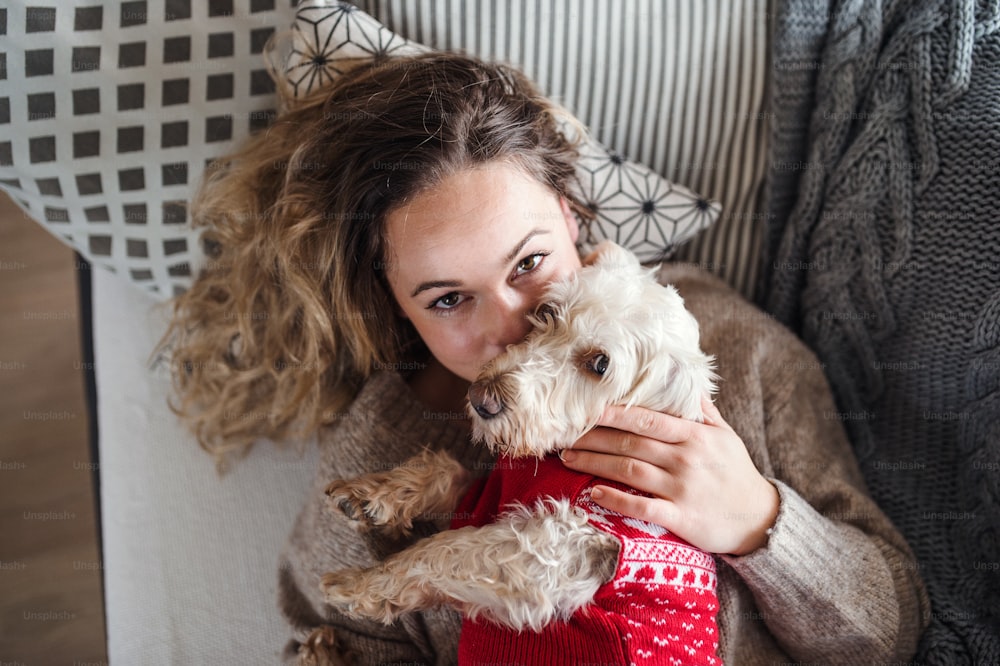 Top view of young woman relaxing indoors on sofa at home with pet dog.