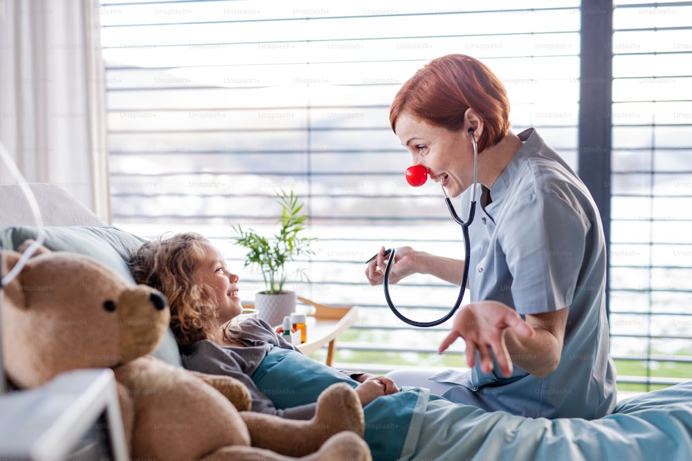 Friendly female doctor with stethoscope examining small girl in bed in hospital.