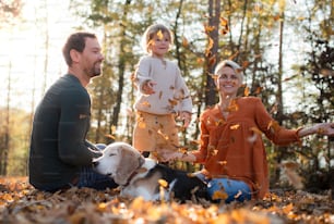 Beautiful young family with small daughter and dog sitting in autumn forest, having fun.