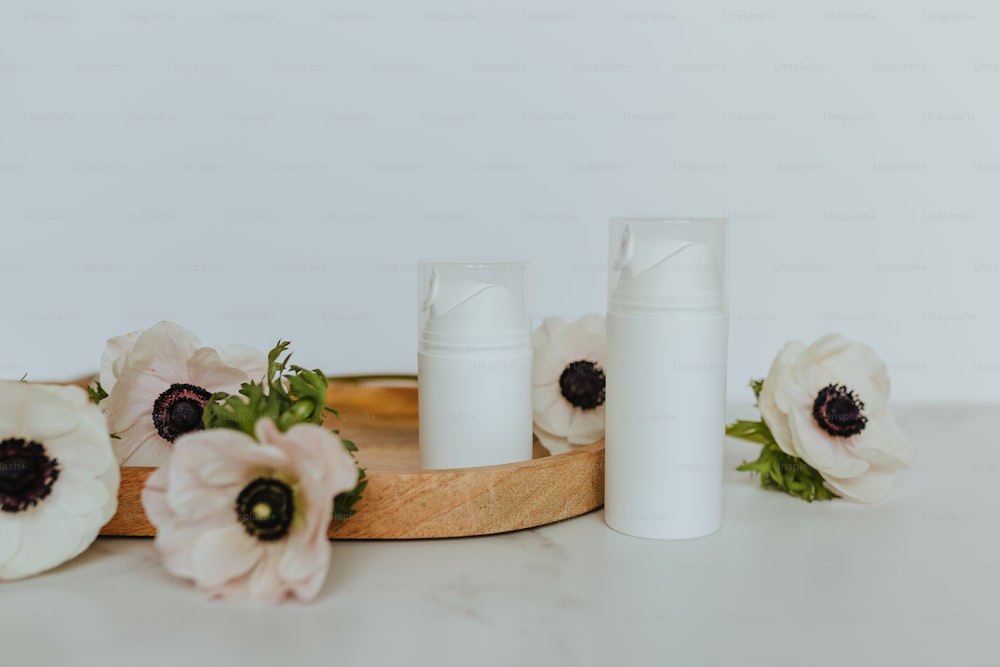 a wooden tray topped with white bottles and flowers