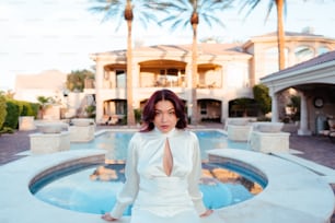 a woman in a white dress standing in front of a pool