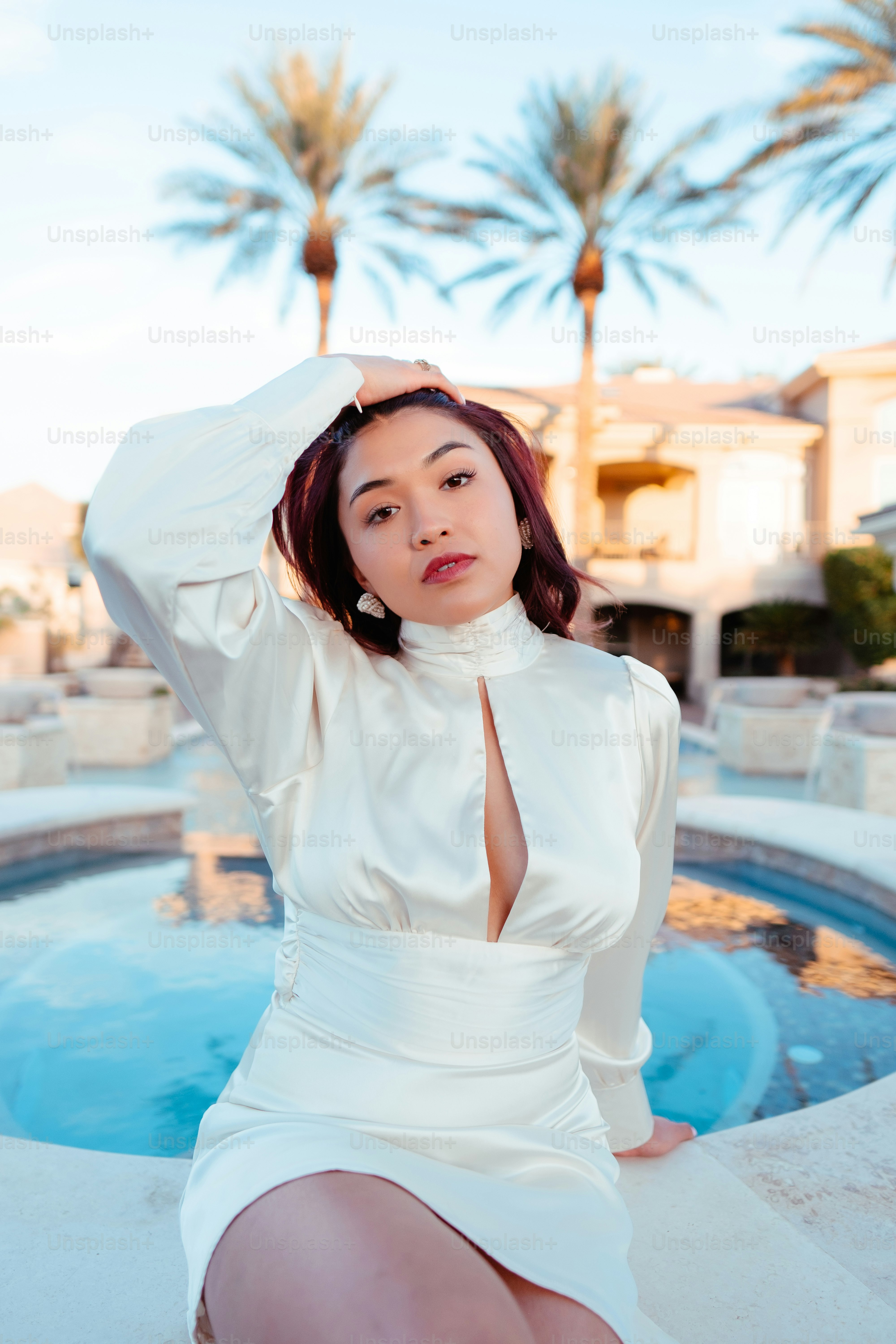Una mujer con un vestido blanco sentada frente a una piscina