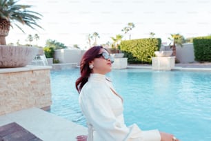 a woman sitting on a ledge next to a pool