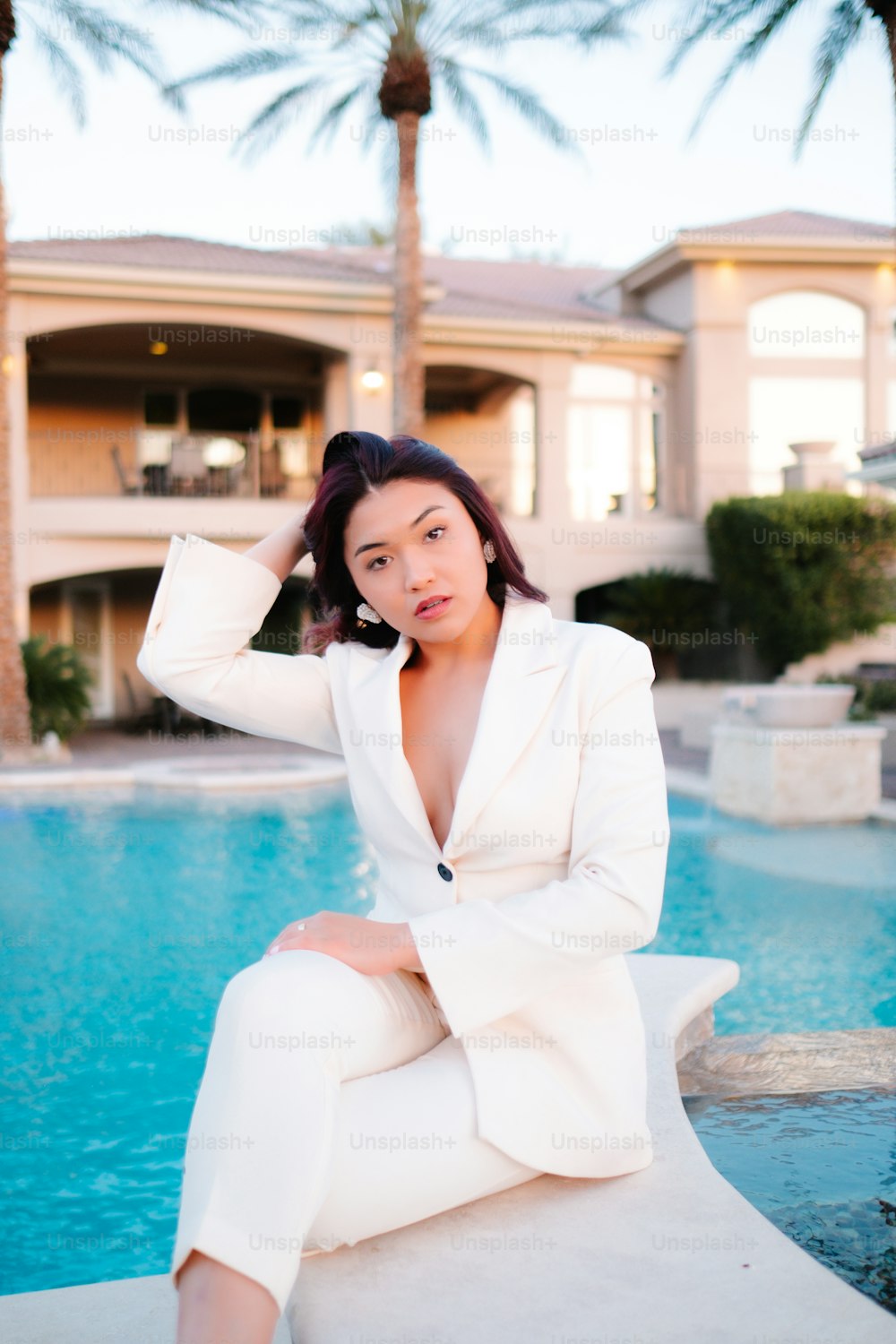 a woman in a white suit sitting by a pool