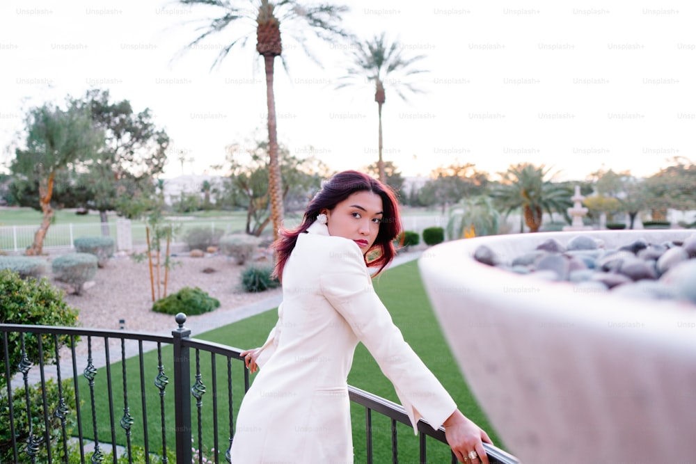 a woman in a white coat leaning on a fence