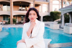 a woman sitting on a ledge next to a pool