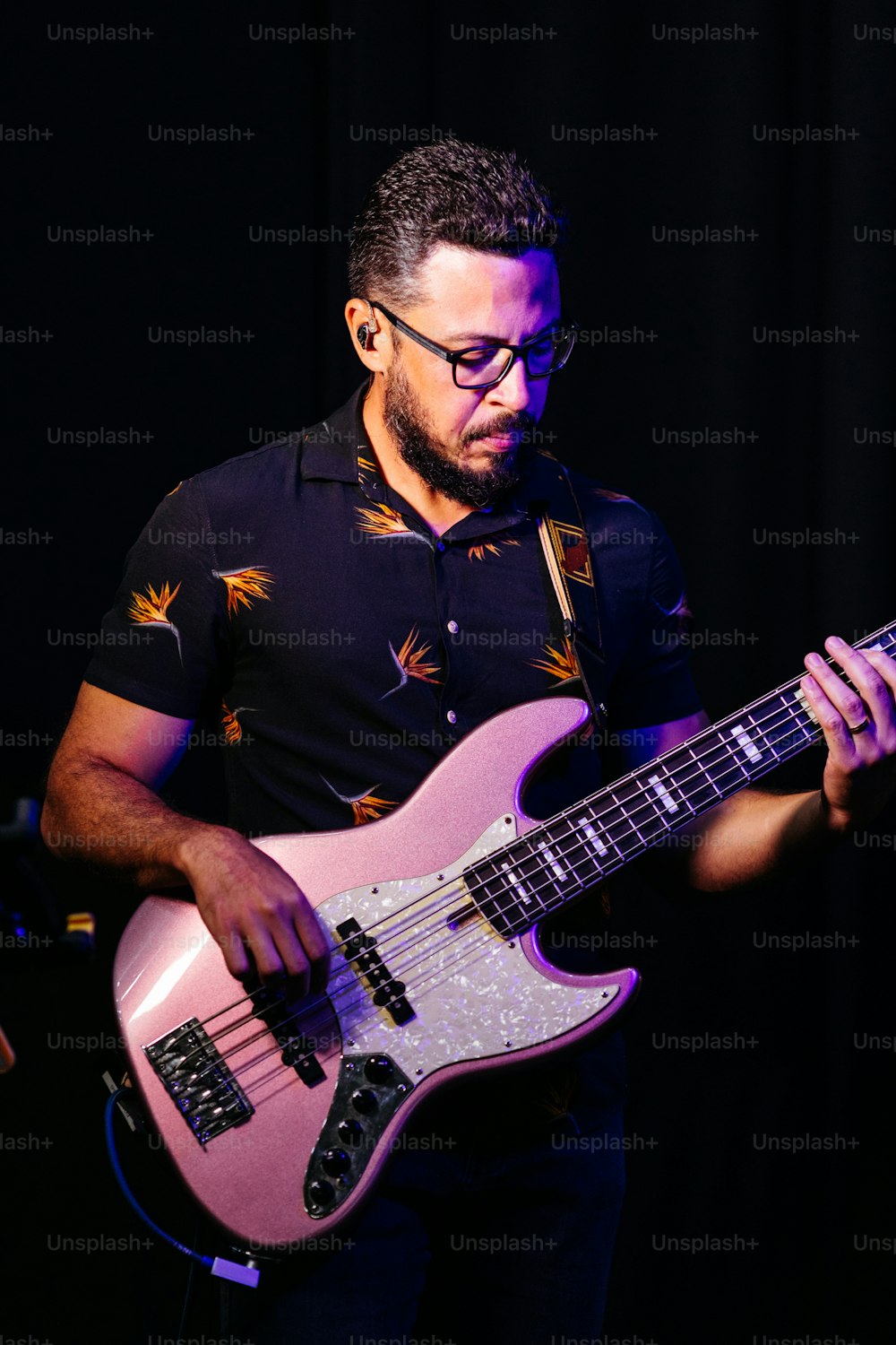 a man with glasses playing a pink guitar