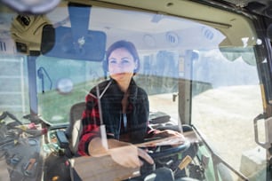 Une ouvrière conduisant un tracteur dans une ferme laitière, dans l’industrie agricole. Tiré à travers le verre.